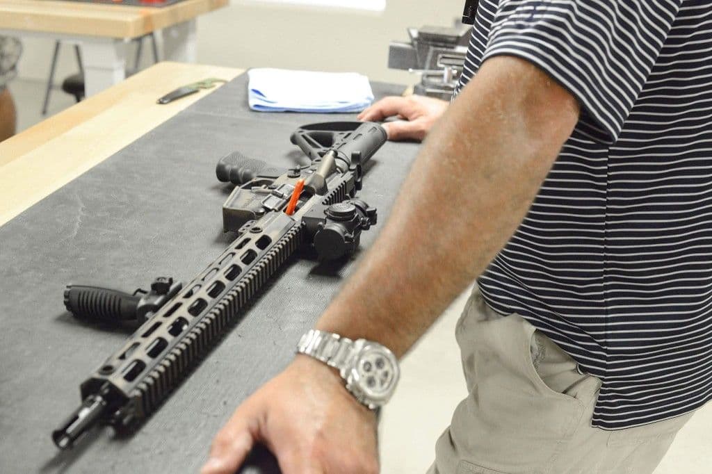 A rifle on a bench with a bright safety chamber flag in the ejection port.